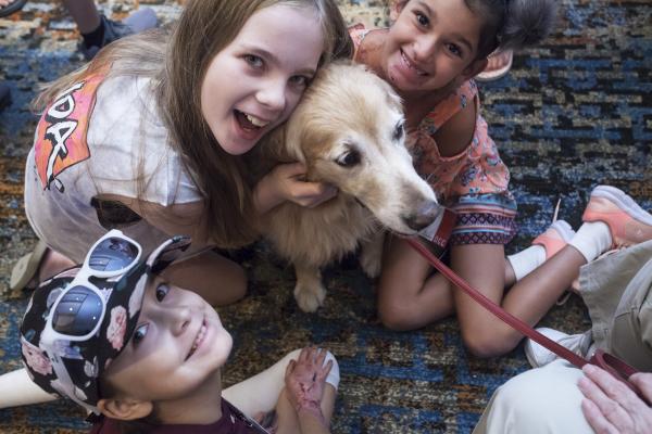 Three girls smiling and holding a dog.